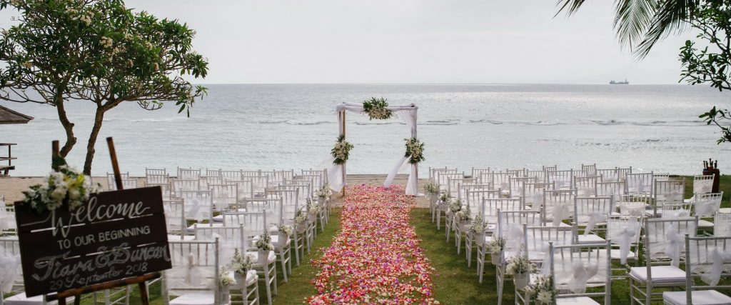 Ceremony set on the beachfront lawn with a petal aisle and floral arch facing the sea at Jeeva Santai Villas, Mangsit Beach, Lombok