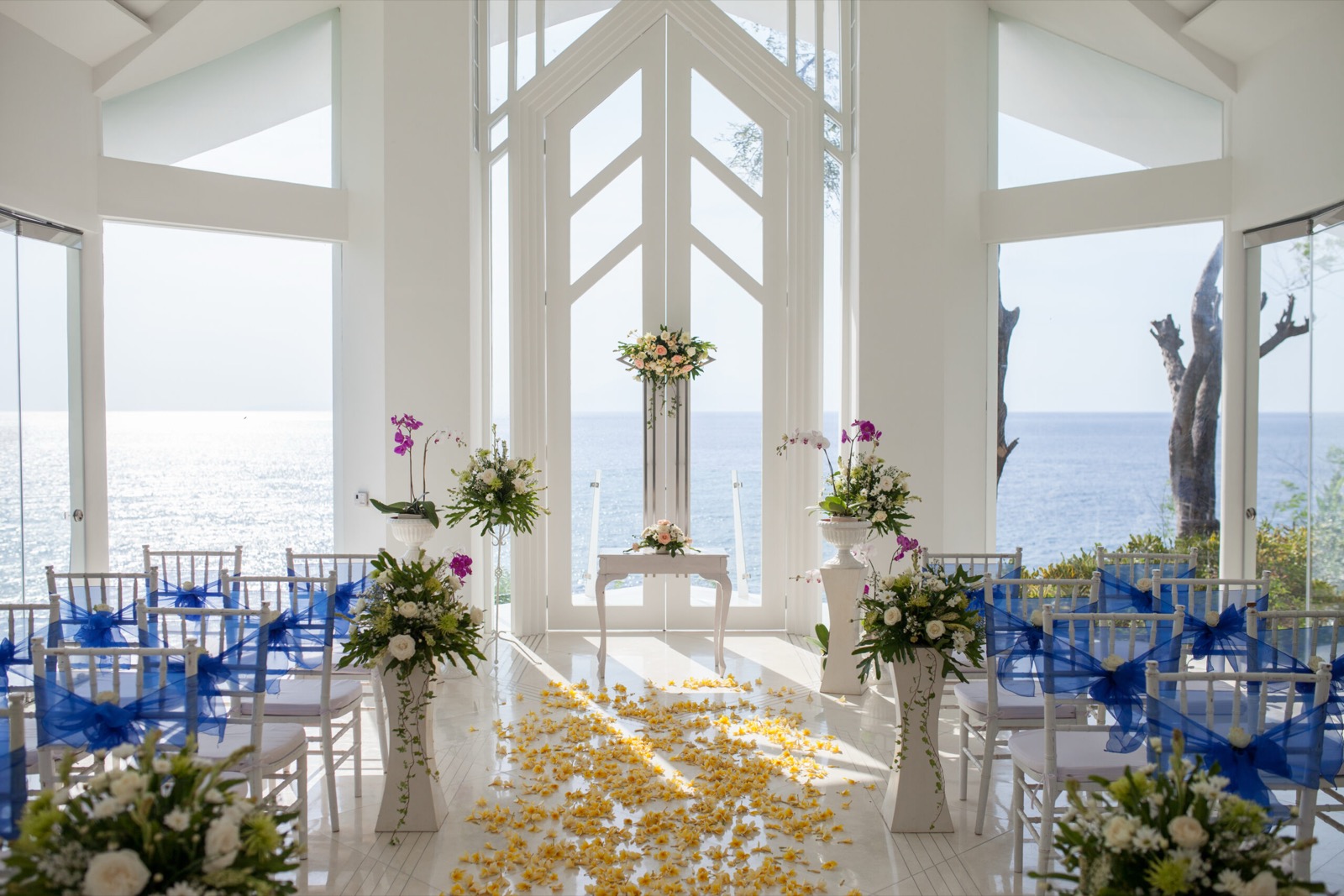 The glass wedding pavilion set with blue chair sashes and a frangipani petal aisle above the sea, Katamaran Resort Lombok