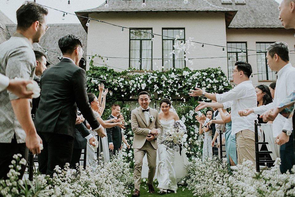 Couple's recessional through a white flower aisle with the villa facade behind at The Kemilau Villa Umalas, Canggu