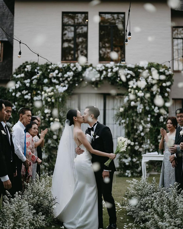 First kiss under a floral arch with the pale European villa behind at The Kemilau Villa Umalas, Canggu