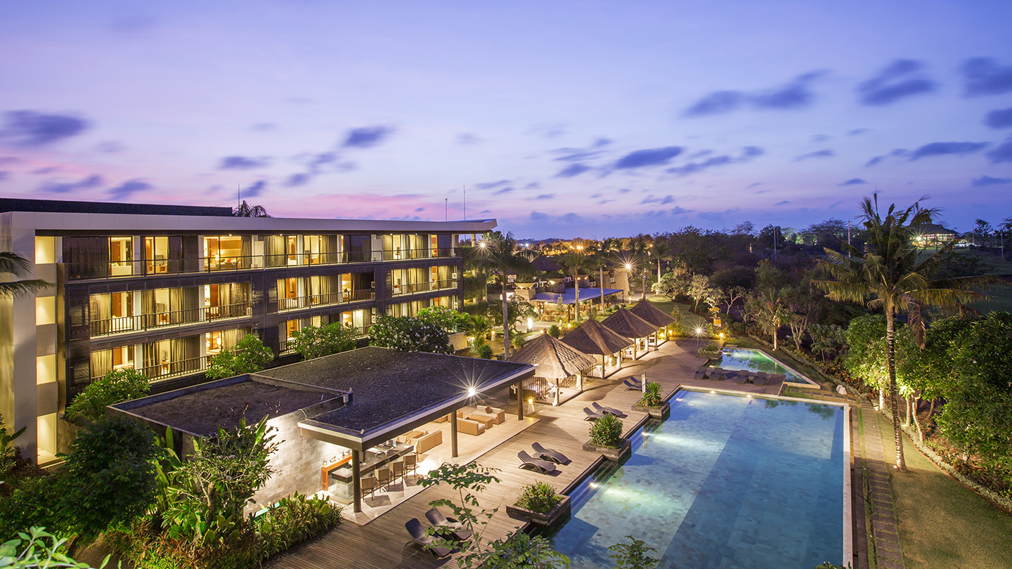 Evening view of Le Grande Bali resort with lit buildings, spa pavilion, and pools overlooking Pecatu, Uluwatu