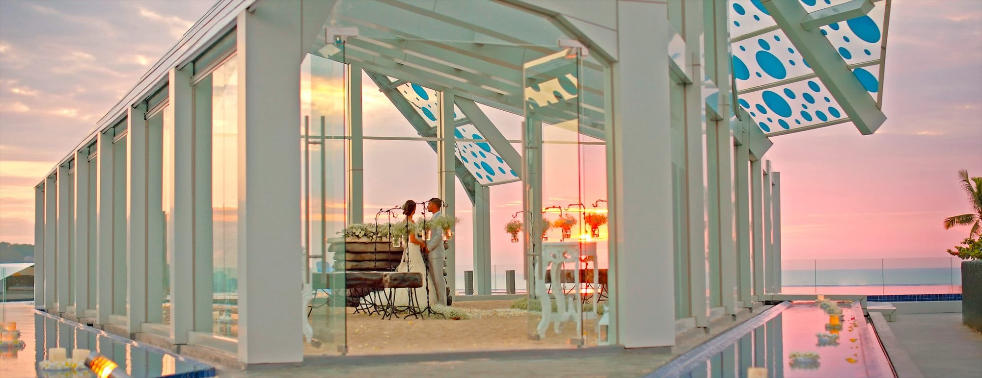 The rooftop Celebration Pavilion glass chapel at Le Meridien Bali Jimbaran at sunset, framed by reflecting pools and ocean beyond