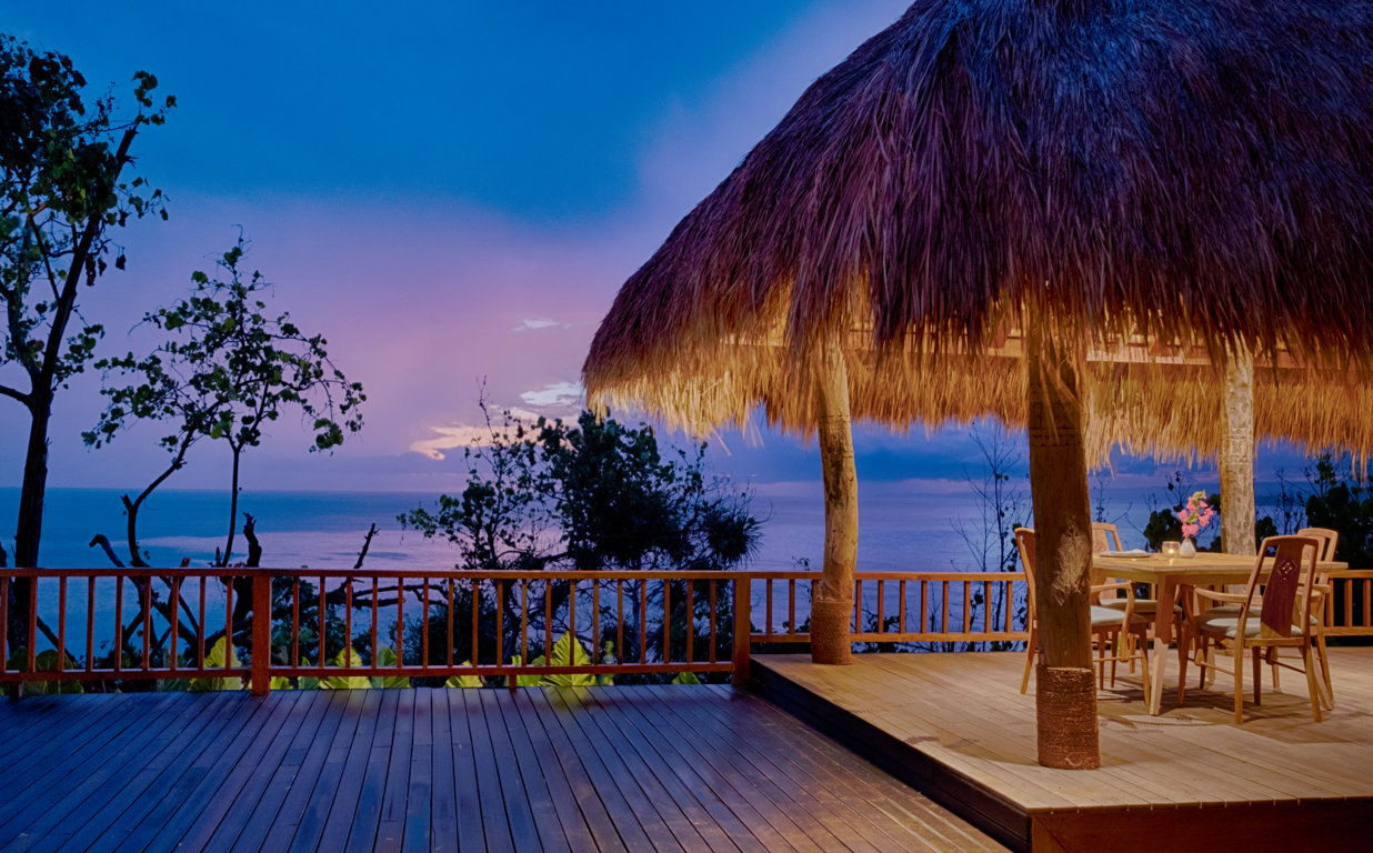Thatched pavilion and deck at dusk with a purple sky over the sea at Lelewatu Resort Sumba, Sumba