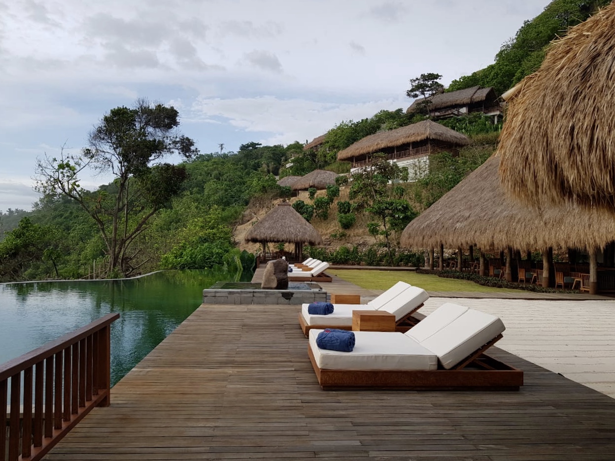 Infinity pool and sun loungers on a timber deck below thatched villas set into the hillside at Lelewatu Resort Sumba on Sumba, one flight from Bali