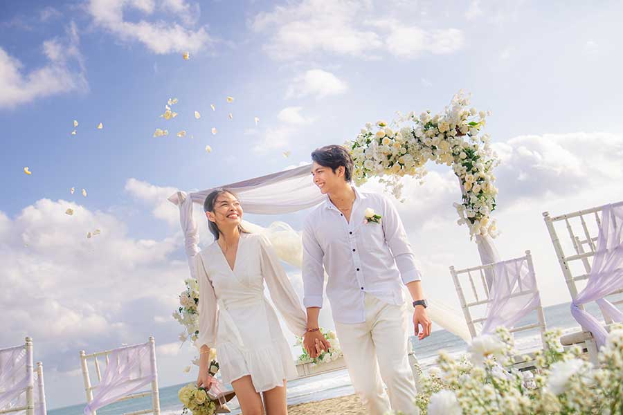 Beachfront wedding ceremony with couple under floral arch on the sand at Lv8 Resort Hotel, Canggu