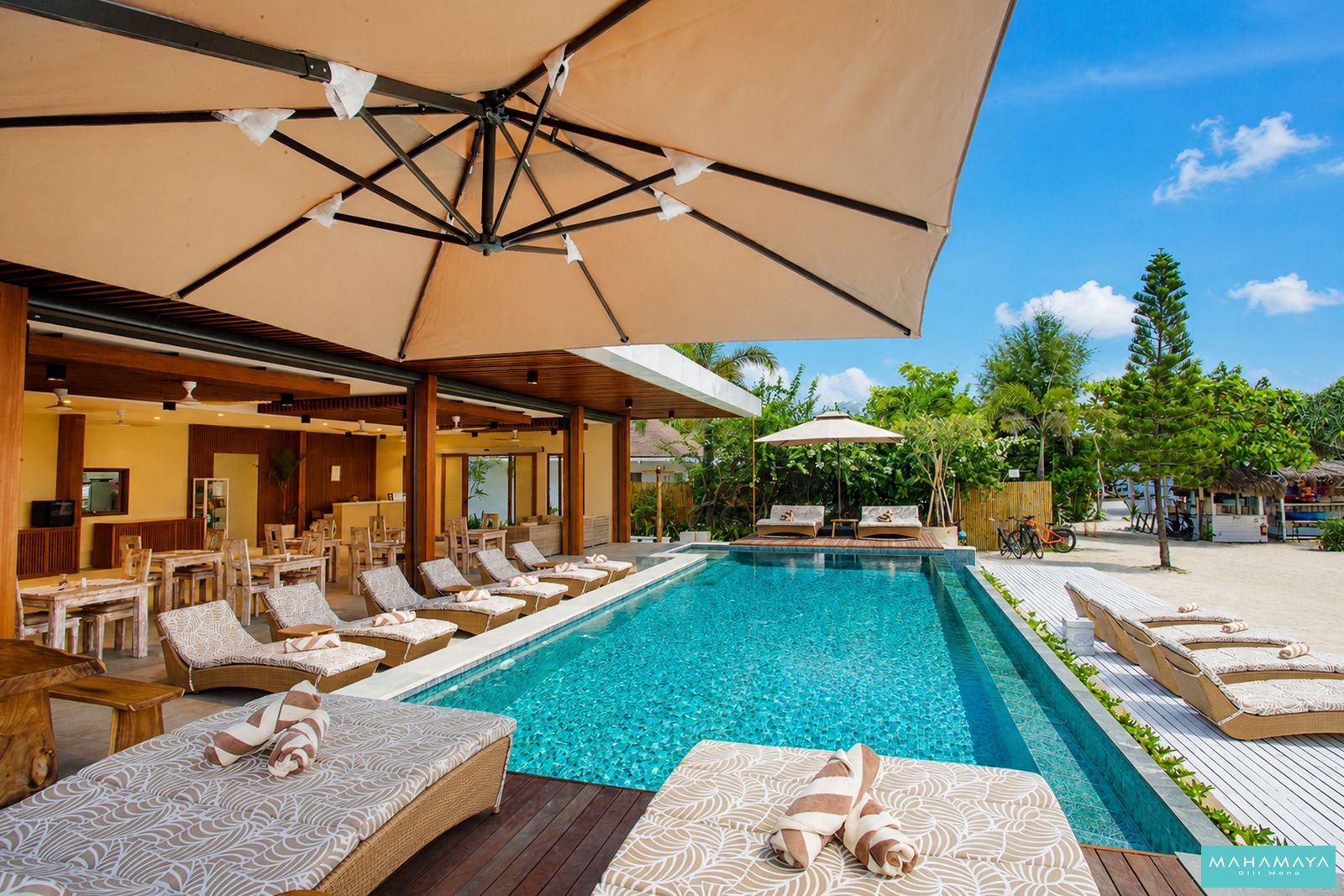 Loungers under cream parasols beside the pool and open restaurant at Mahamaya Gili Meno, Gili Meno