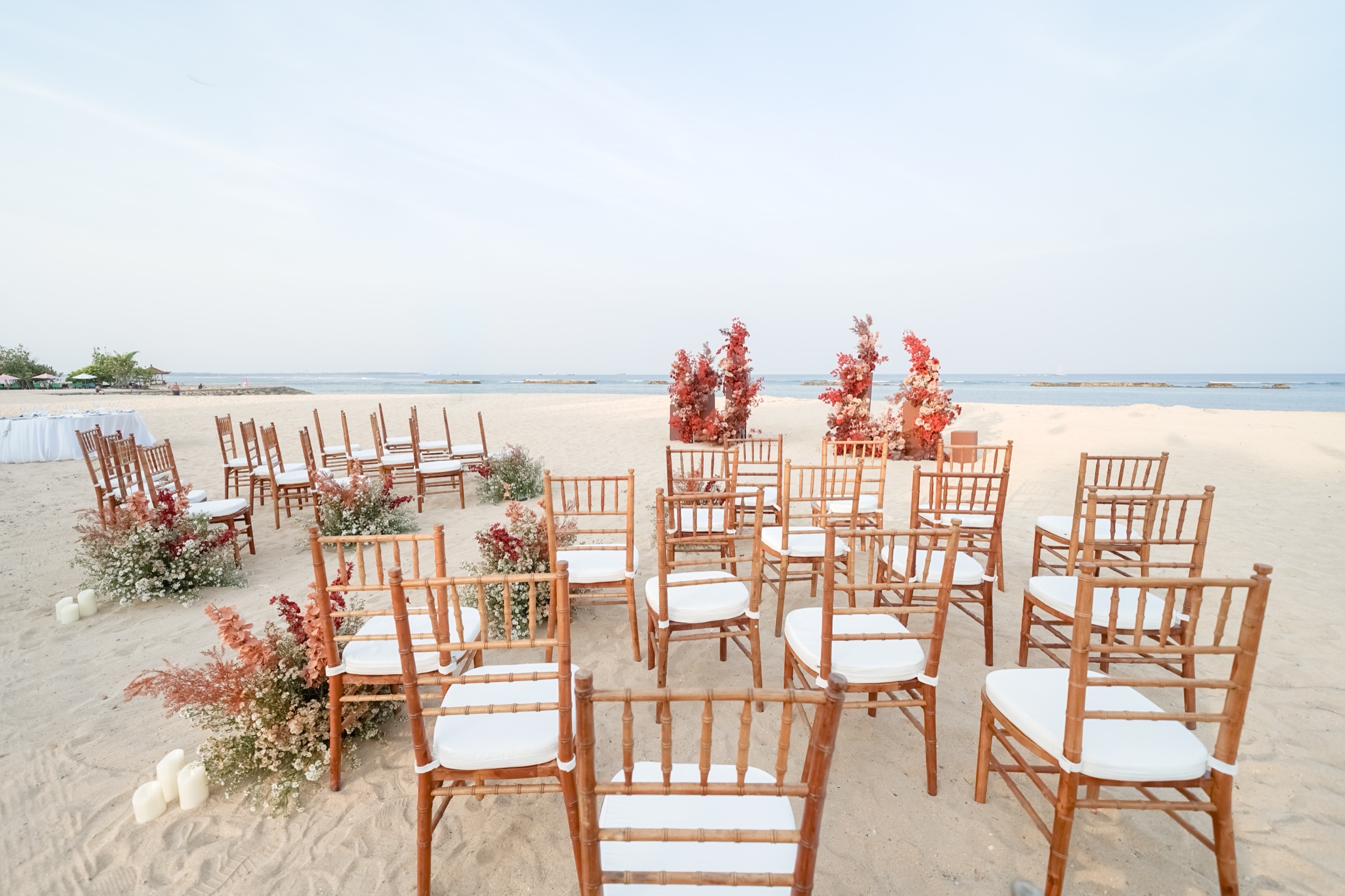 A beach ceremony set with timber chairs and floral styling on the sand at Manarai Beach House, Nusa Dua