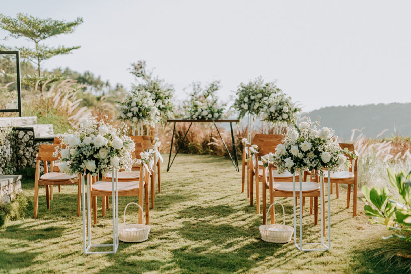 Ceremony aisle with white florals and teak chairs in golden light at MAUA Nusa Penida on Nusa Penida, Bali