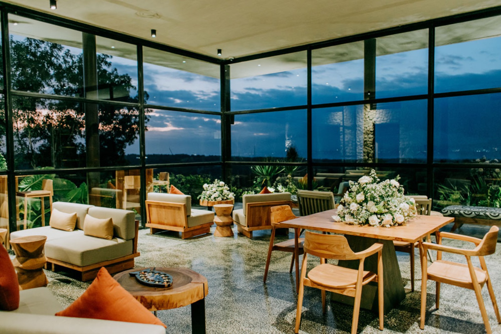 Glass-walled lounge dressed with wedding florals at dusk at MAUA Nusa Penida, Bali