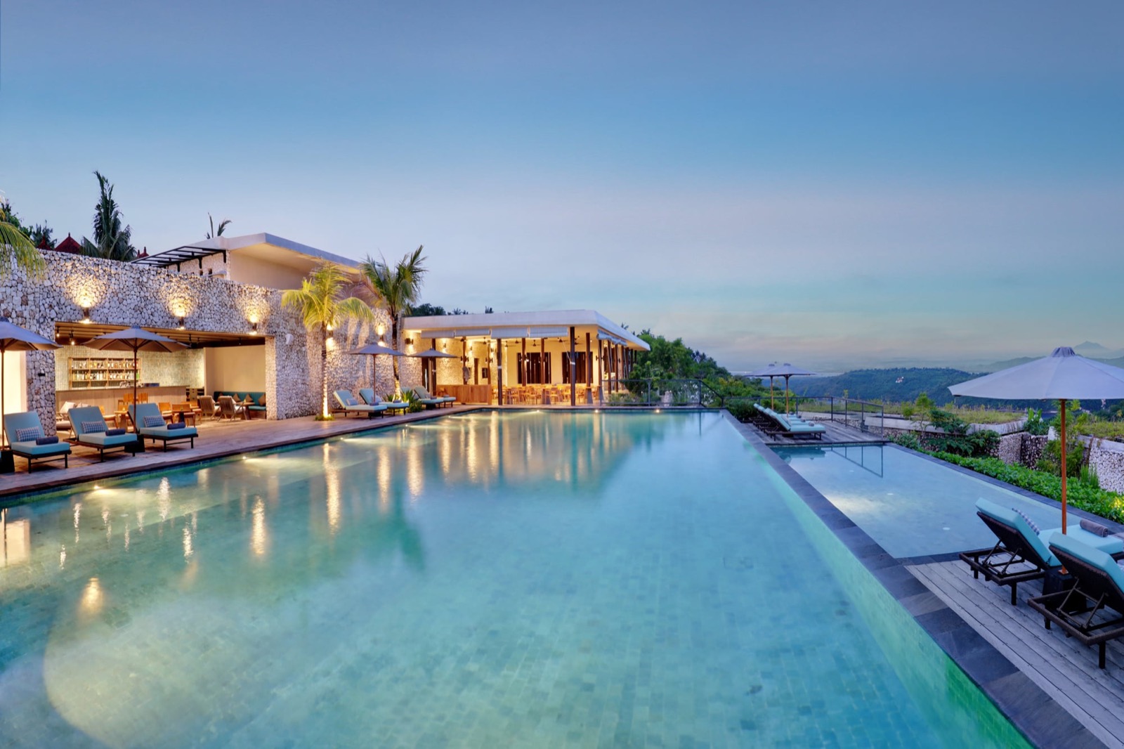 Main pool with the Aroha bar and Kowhai restaurant lit at dusk at MAUA Nusa Penida, Bali