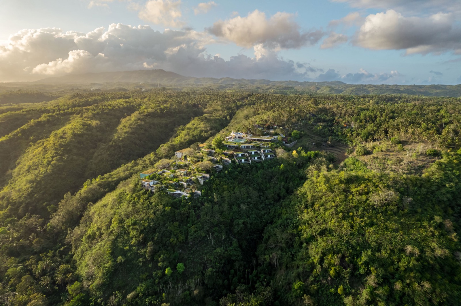Aerial view of the MAUA Nusa Penida villas set into a green ridge on Nusa Penida, Bali