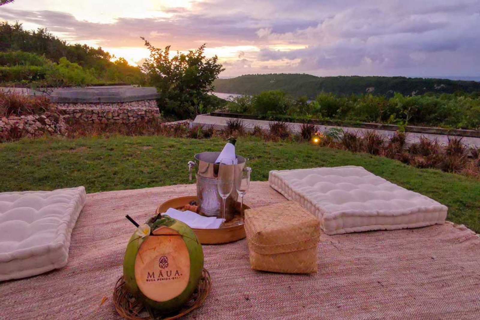 Sunset picnic with champagne and cushions facing Gamat Bay at MAUA Nusa Penida, Bali