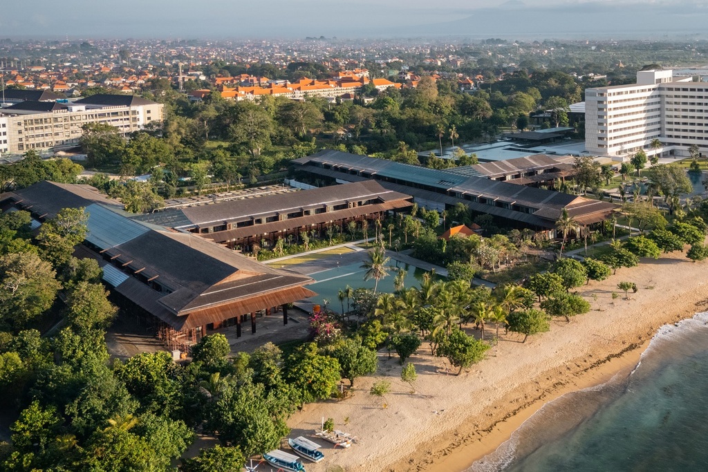 Aerial view of The Meru Sanur's low pavilions and gardens meeting the golden sand of Sanur Beach