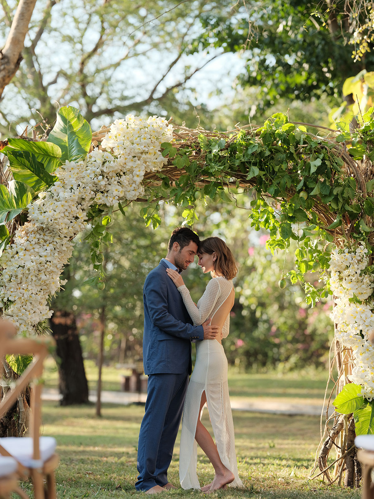 Couple standing under a frangipani and vine arch in the tropical garden at Mimpi Resort Tulamben in northeast Bali