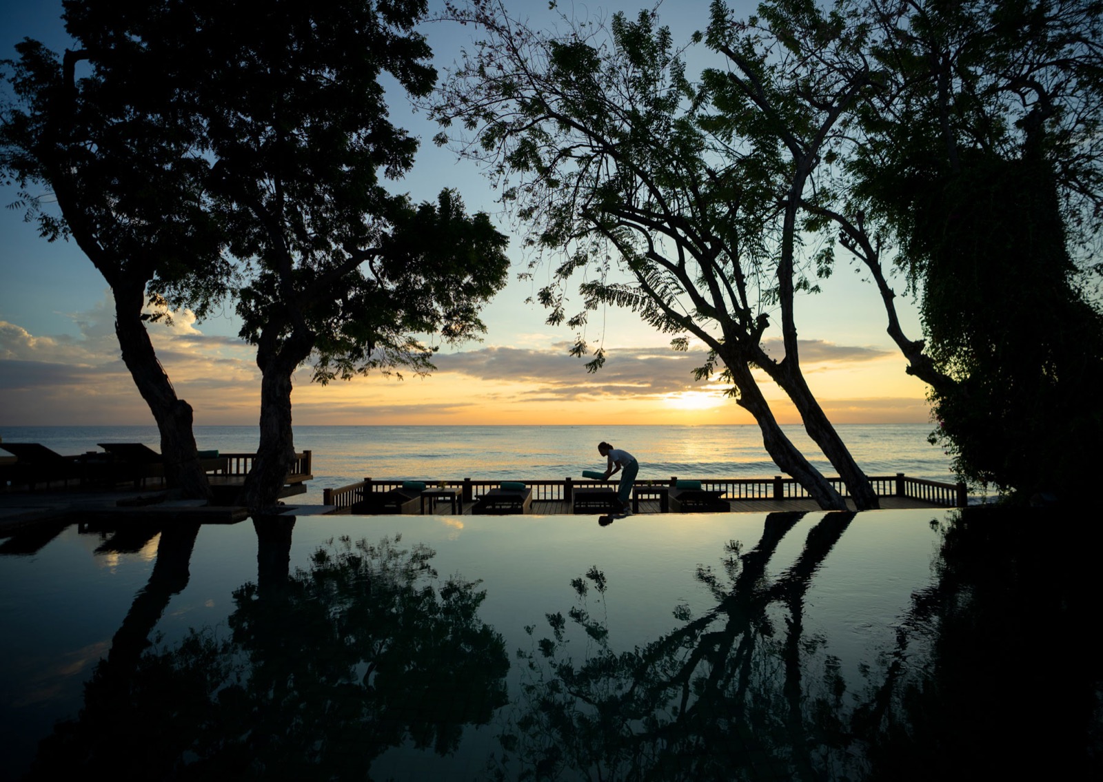 Low sun over the sea seen across the infinity pool and beachfront deck at Mimpi Resort Tulamben in northeast Bali