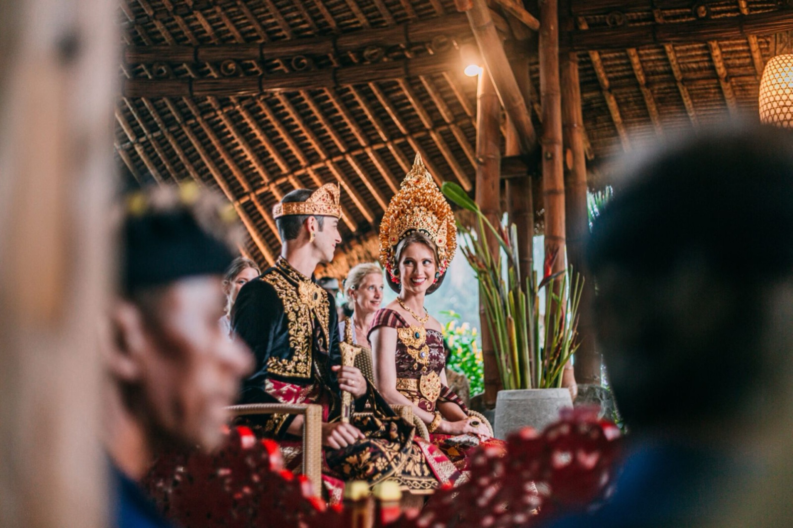Bride and groom in gold Balinese headdresses seated under the bamboo roof during their blessing at Munduk Moding Plantation, Munduk, Bali