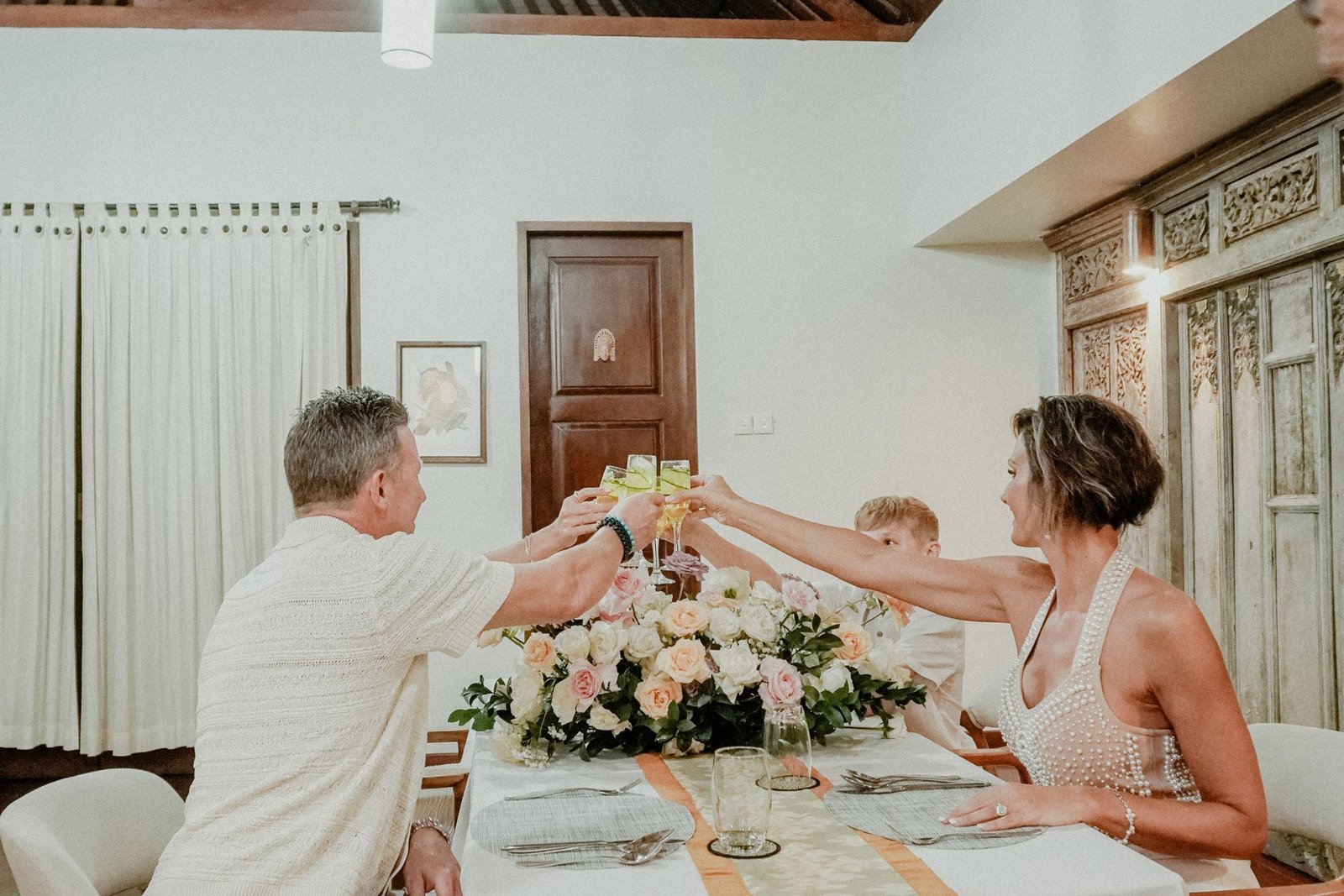 Couple and guests raising a toast over a rose centrepiece at a private wedding dinner at Munduk Moding Plantation, Munduk, Bali
