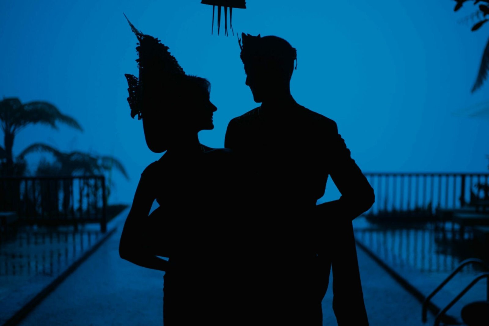 Silhouette of a couple in Balinese headdresses beside the pool at dusk, Munduk Moding Plantation, Munduk, Bali