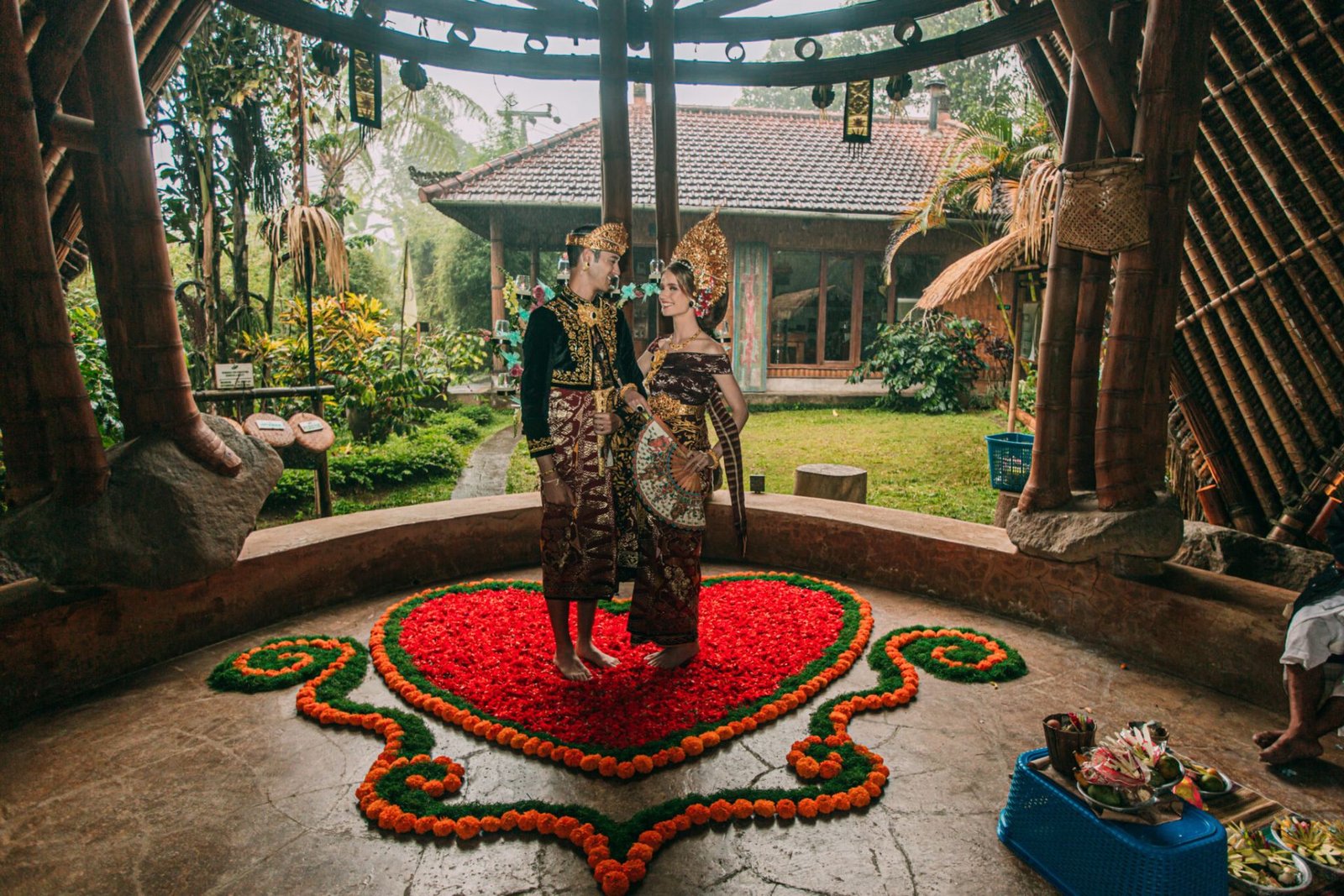 Couple in traditional Balinese wedding dress standing on a heart of marigolds inside the bamboo pavilion at Munduk Moding Plantation in the Munduk highlands of Bali