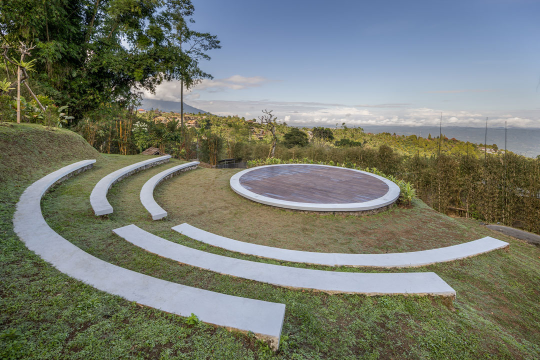 The grass amphitheatre with curved concrete benches and a round timber stage cut into the ridge at Munduk Tentrem, Munduk, Bali