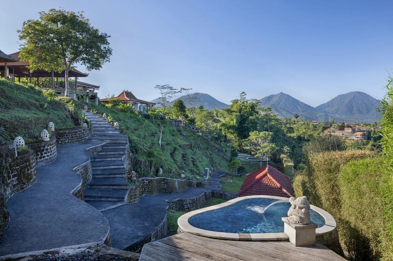 Stone steps winding down past a small round pool with the mountains behind at Munduk Tentrem, Gobleg, Bali