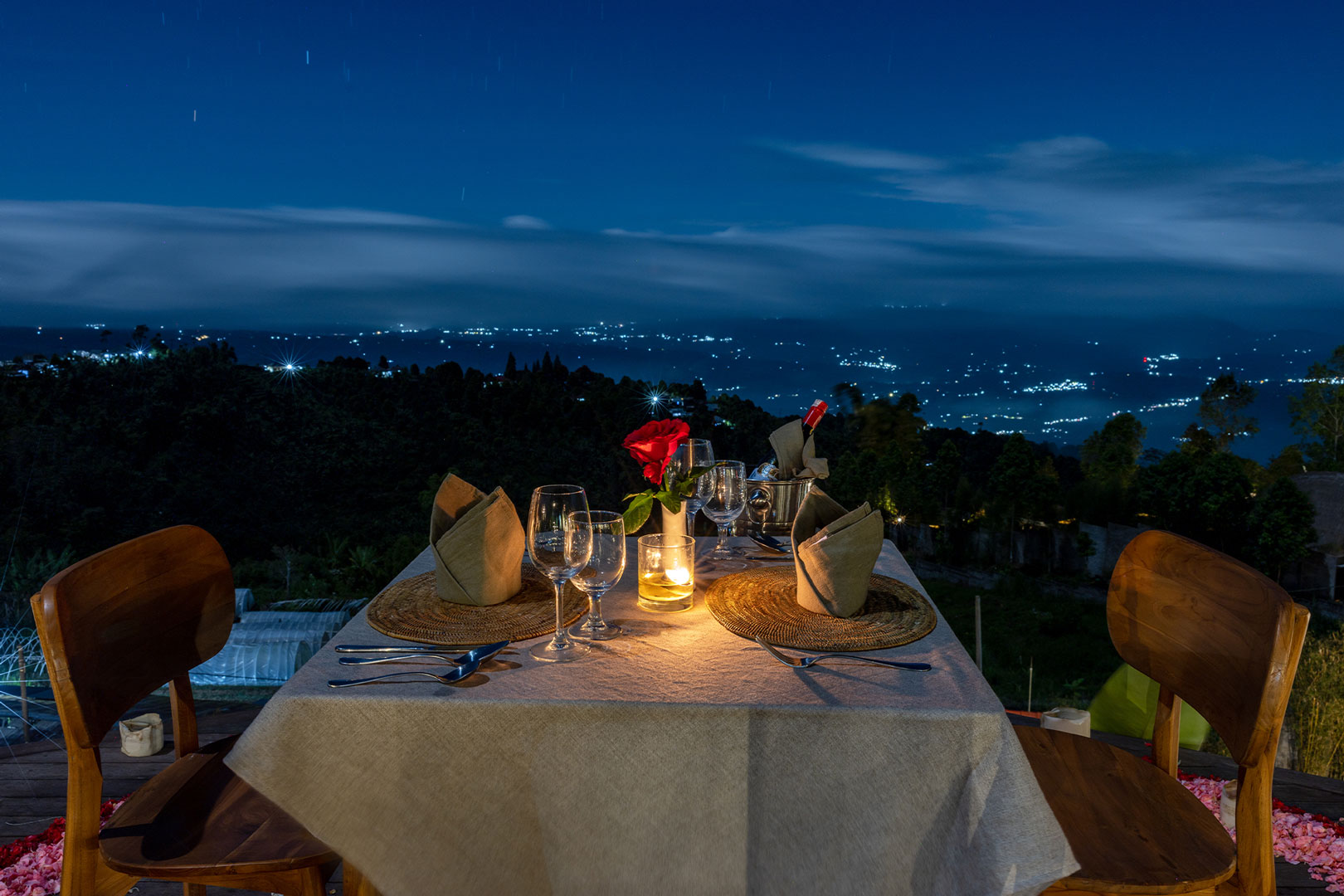 Candlelit table for two on a deck at night above the lights of the north Bali coast at Munduk Tentrem