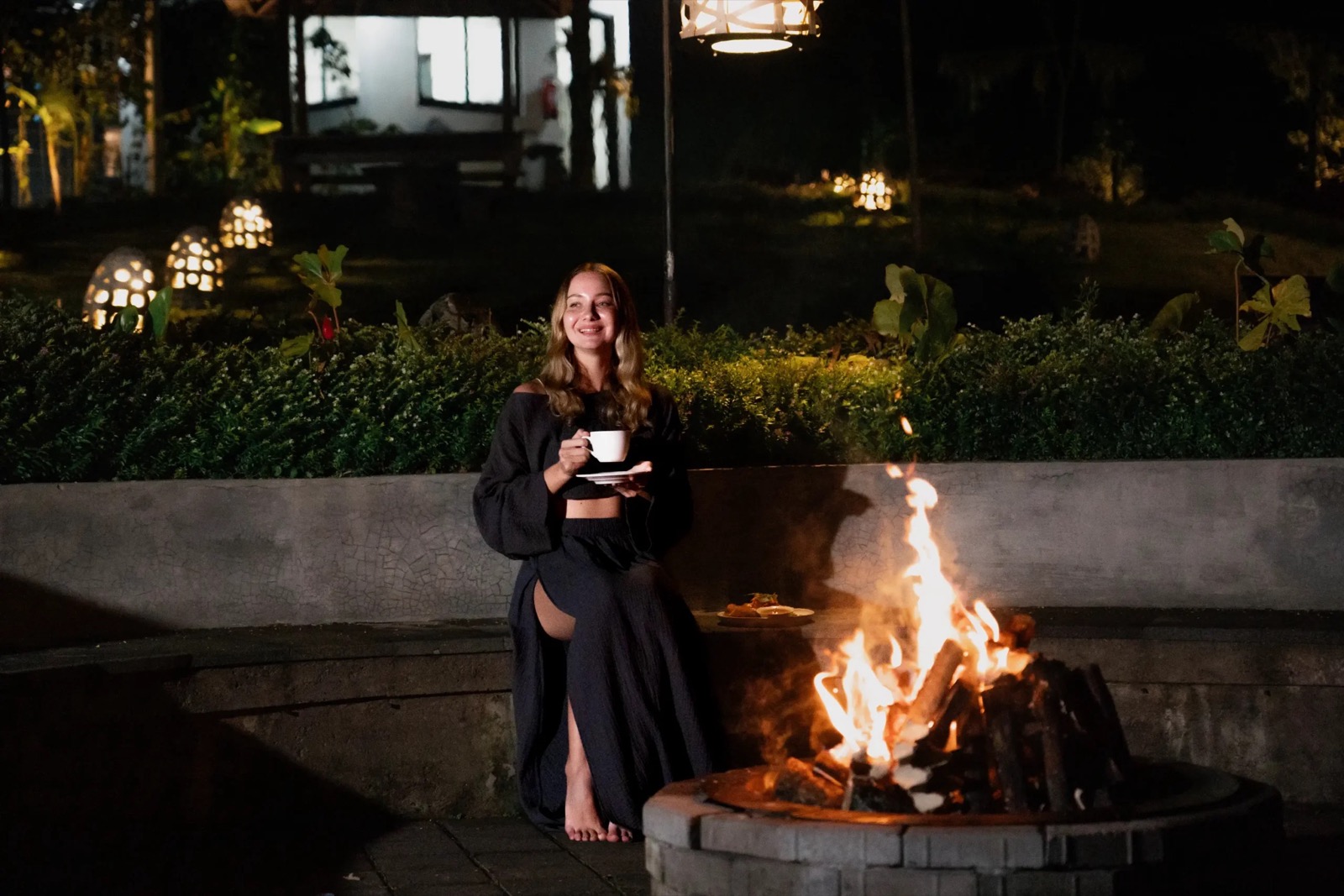 Guest sitting by the lit fire pit with lanterns in the garden after dark at Munduk Tentrem, Munduk, Bali