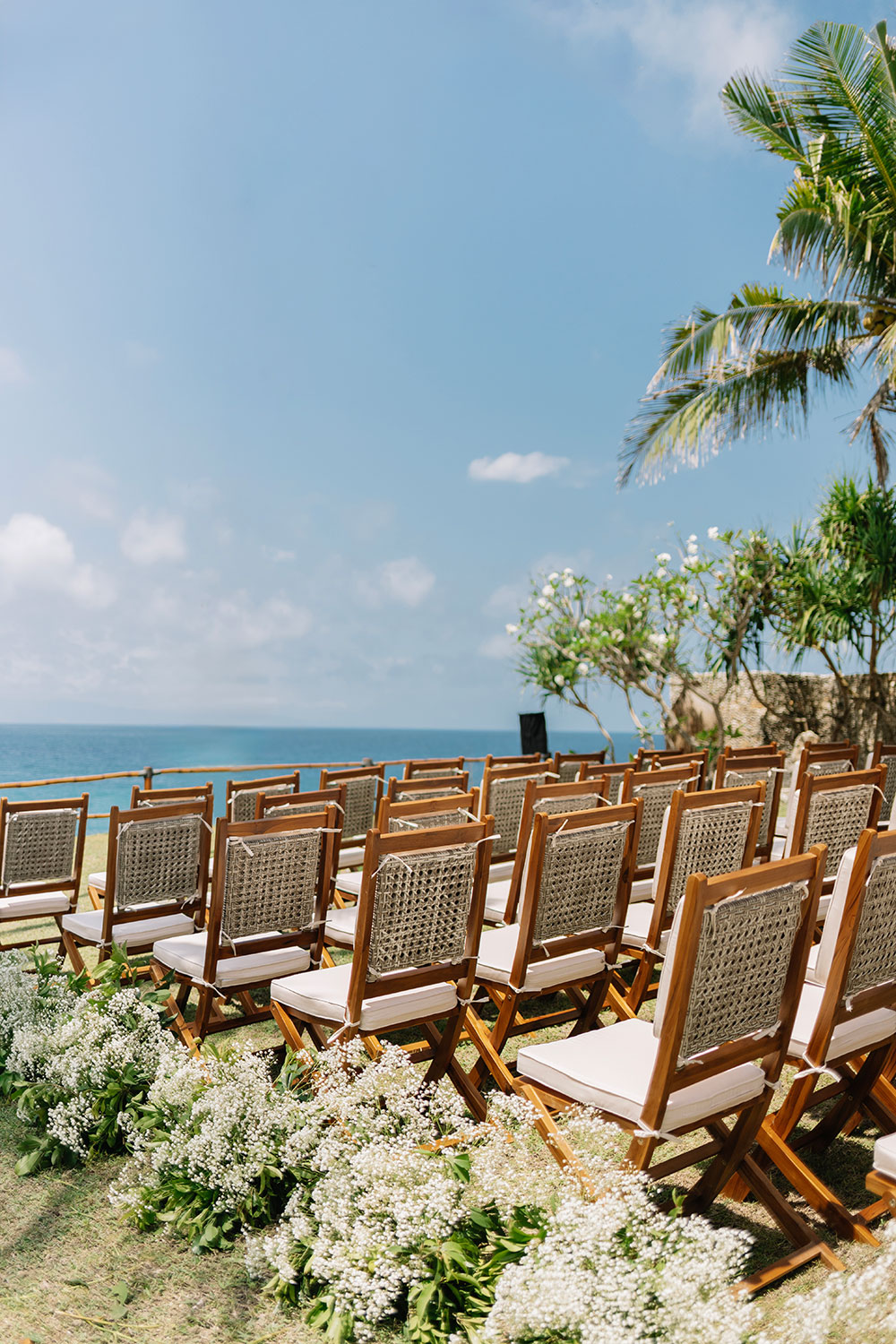 Rows of teak ceremony chairs lined with white florals above the sea at NIHI Sumba, Sumba