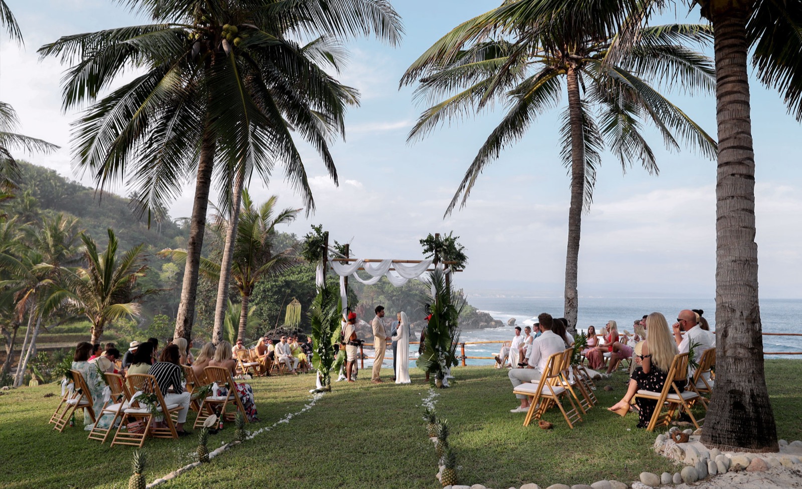 Wedding ceremony on the clifftop lawn under coconut palms above the ocean at NIHI Sumba on Sumba