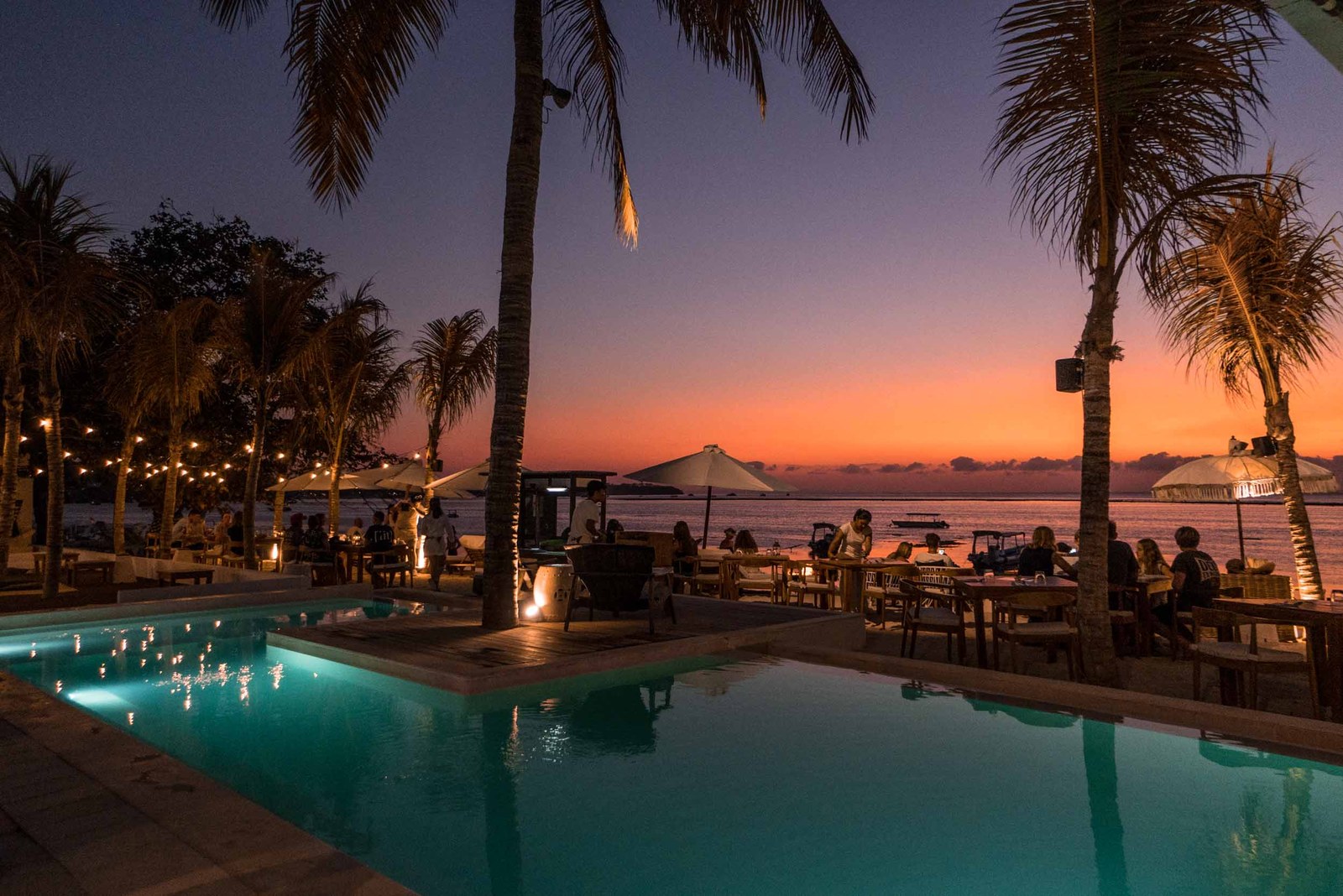 Beachfront pool at sunset framed by palms at Ohana's Beachfront Resort on Nusa Lembongan, Bali