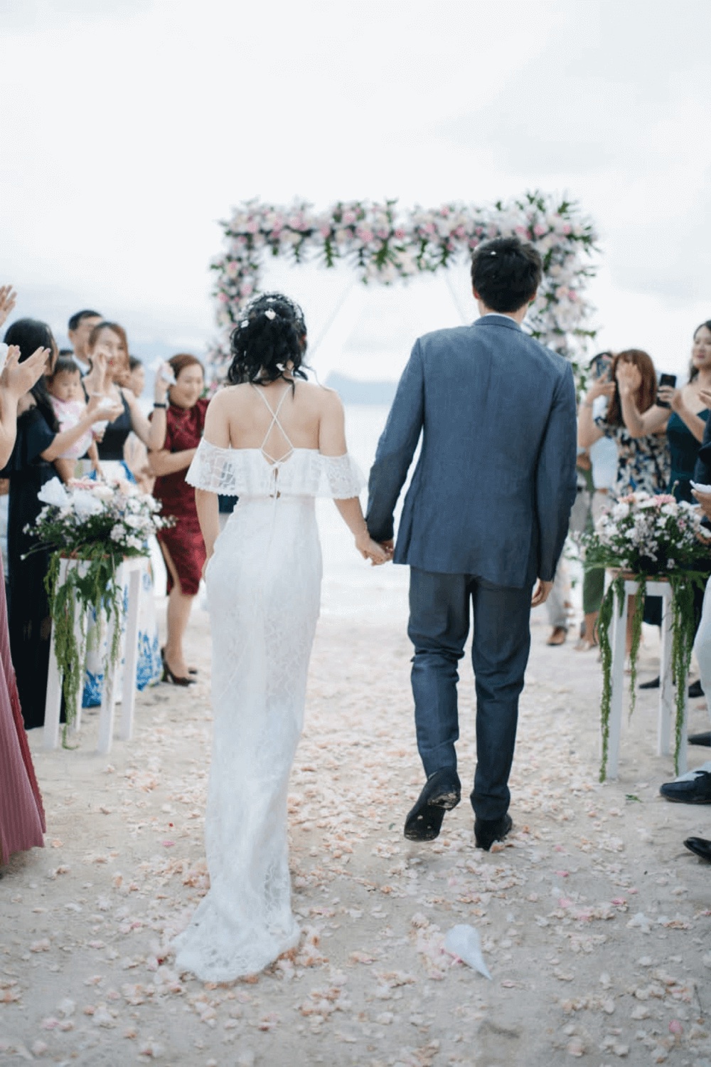 Bride and groom walking the petal-strewn aisle towards a pink and white floral arch on the beach at Pondok Santi Estate, Gili Trawangan