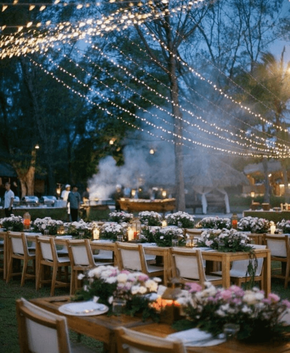 Long timber dinner tables under canopies of festoon lights in the coconut grove at Pondok Santi Estate, Gili Trawangan