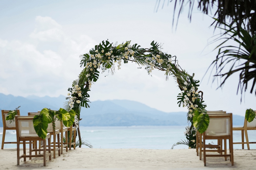 Ceremony arch of white blooms and tropical foliage framing the sea and the Lombok coastline at Pondok Santi Estate, Gili Trawangan