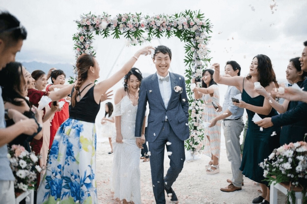 Newlyweds walking back down the sand aisle through a shower of petals under a floral arch at Pondok Santi Estate on Gili Trawangan, off Lombok