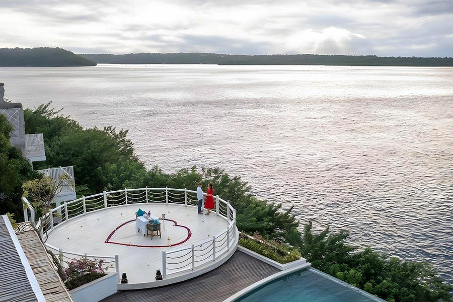 Couple on the round cliff-edge deck of the Natura Chapel above the Toyapakeh strait at Pramana Natura Nusa Penida, Bali