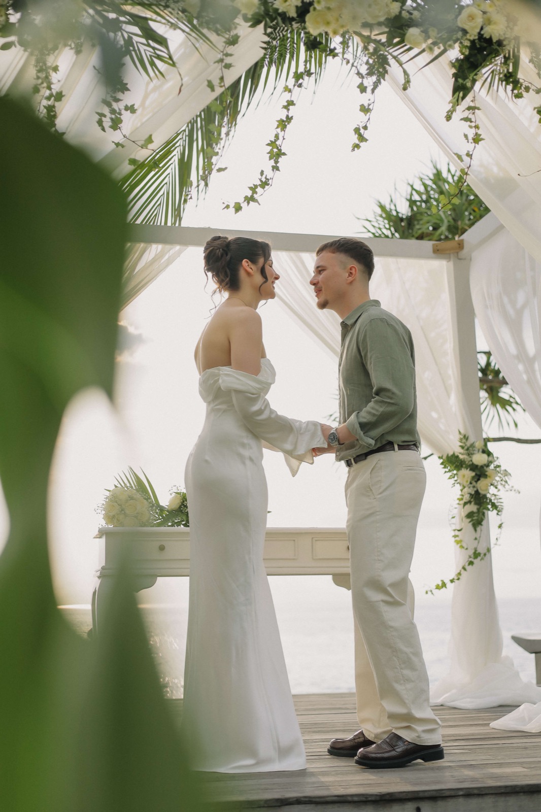 Bride and groom holding hands under a white draped pavilion trimmed with greenery at Qunci Villas, Mangsit Beach, Lombok