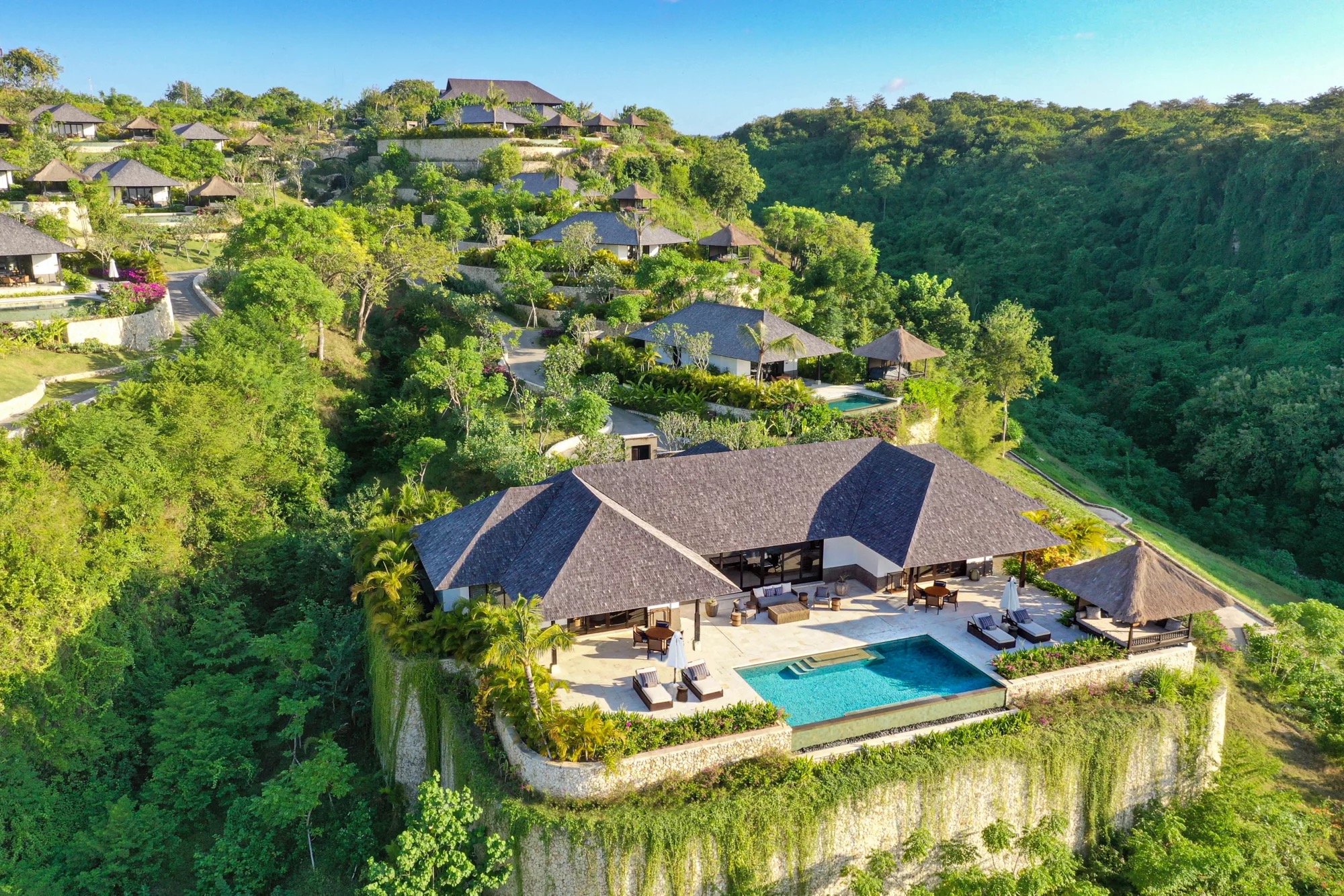 Aerial view of Raffles Bali's terraced hillside villas with private pools set into green cliffs above Jimbaran Bay