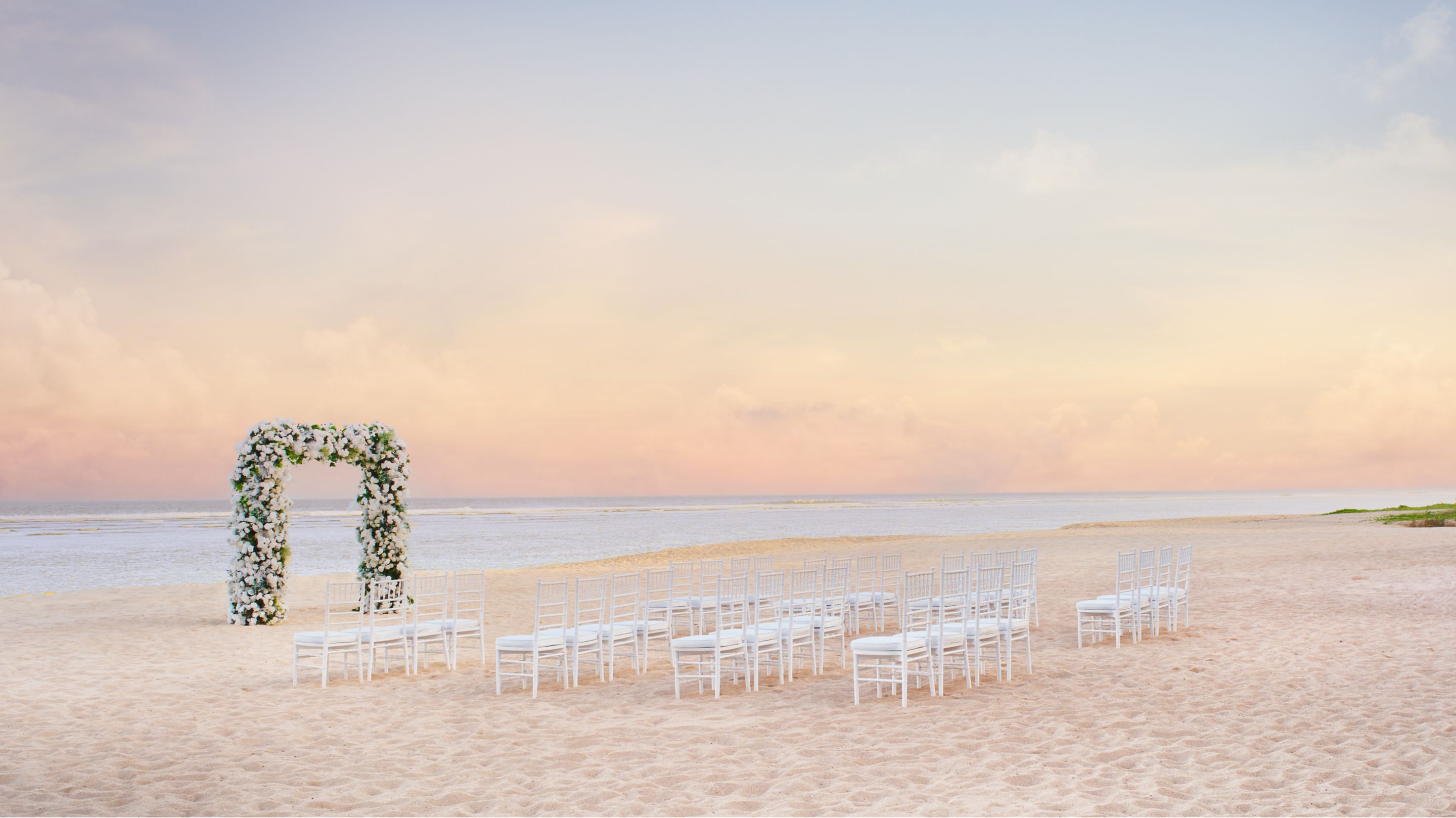 A beachfront ceremony set with an arch and white chairs on the sand at The Ritz-Carlton, Bali
