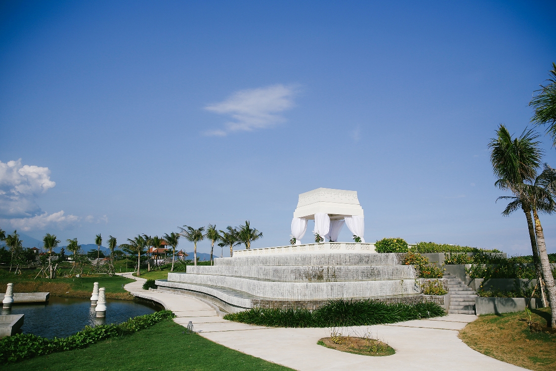 The white draped wedding pavilion on its terraced platform above a pond at Rumah Luwih Beach Resort, Gianyar, with palms and mountains behind
