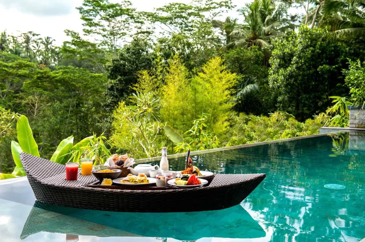 Floating breakfast in a boat-shaped object over turquoise pool with rainforest backdrop at Samsara Ubud