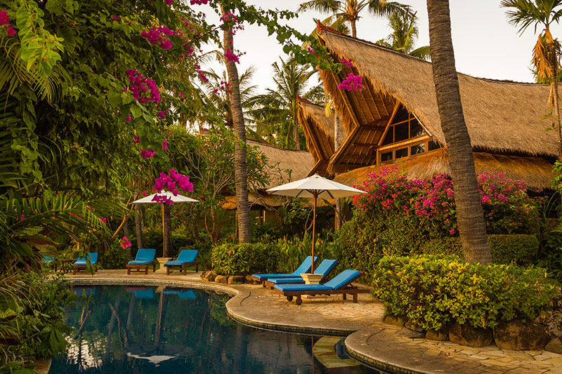 Pool, sun loungers and thatched Toraja-style cottages among bougainvillea and coconut palms at Santai Hotel Amed in east Bali