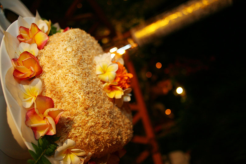 Coconut wedding cake ringed with frangipani and roses under evening lights at Santai Hotel Amed in east Bali