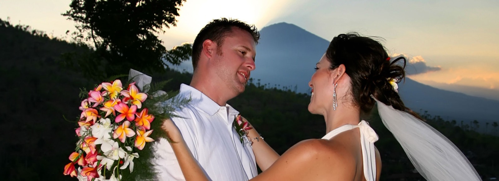 Bride and groom laughing together at sunset with Mount Agung behind them at Santai Hotel Amed on the Amed coast in east Bali