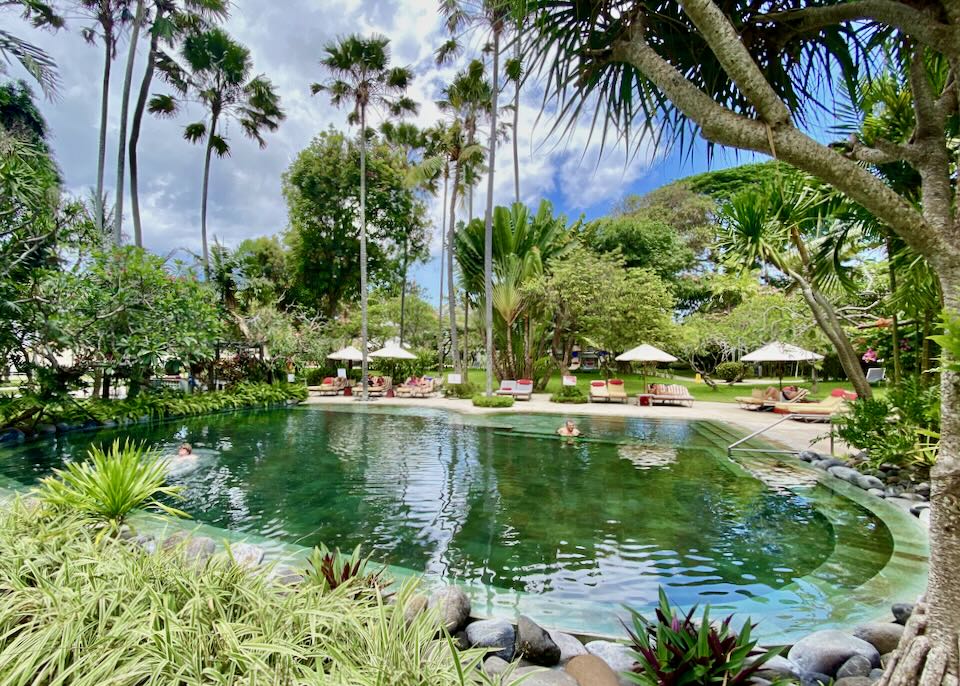 The lagoon-style pool framed by tall palms and thatched umbrellas in the gardens of Segara Village Hotel, Sanur