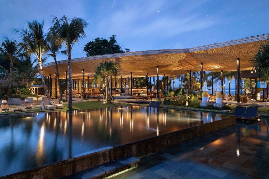 Beachfront restaurant pavilion with teak roof and evening lighting reflected in shallow water pool at Segara Village Hotel, Sanur