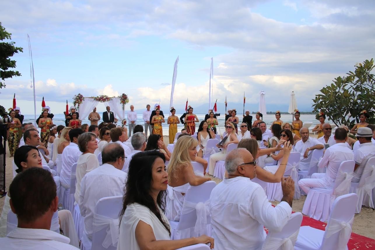 Beach wedding ceremony with white chairs, a floral arch and Sasak dancers in traditional dress at Seri Resort Gili Meno