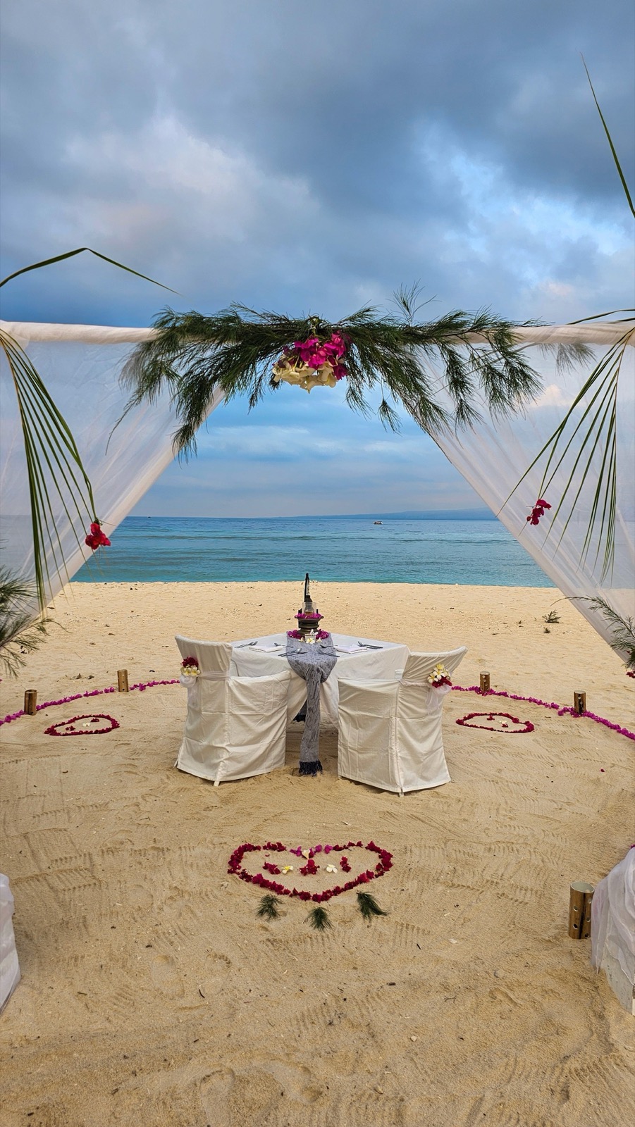 Private dinner for two under a draped arch with petal hearts on the sand at Seri Resort Gili Meno