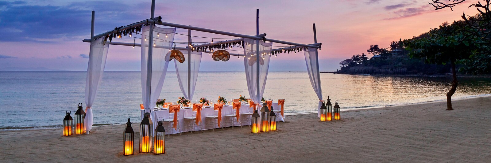 Draped beach canopy over a long dinner table lit by lanterns at dusk on Senggigi Beach, Sheraton Senggigi Beach Resort