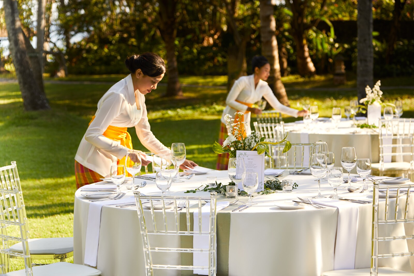 Staff laying round dinner tables on the garden lawn under palms at Sheraton Senggigi Beach Resort, Senggigi