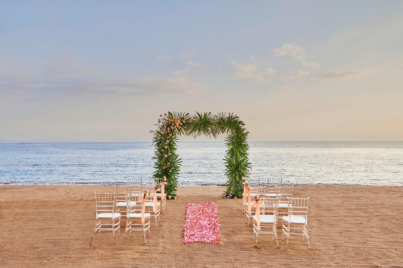 Beach ceremony set with a tropical arch and pink petal aisle facing the water at Sheraton Senggigi Beach Resort, Lombok